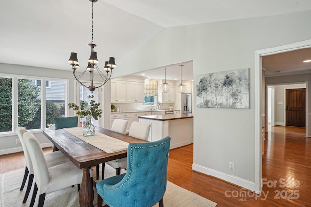 dining room with a chandelier, lofted ceiling, baseboards, and wood finished floors