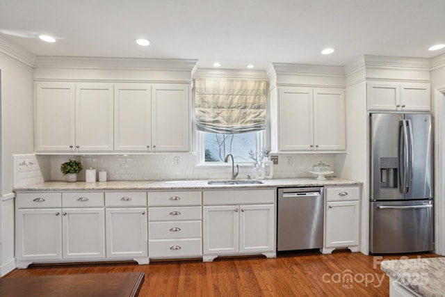 kitchen with white cabinets, appliances with stainless steel finishes, wood finished floors, light stone countertops, and a sink