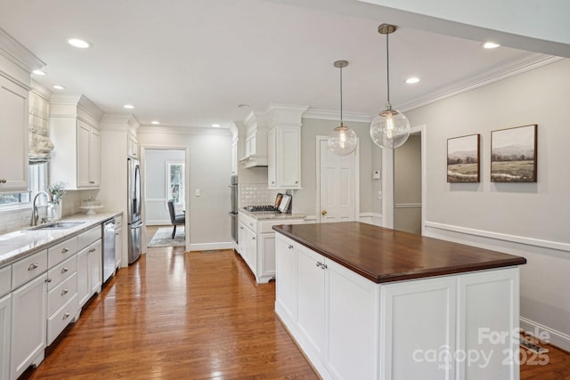 kitchen featuring stainless steel appliances, wood finished floors, a sink, white cabinetry, and tasteful backsplash