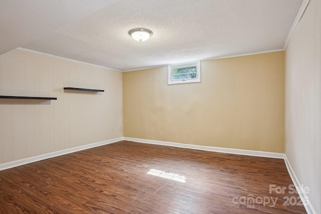 spare room featuring a textured ceiling, ornamental molding, wood finished floors, and baseboards