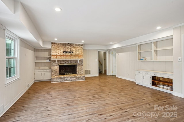 unfurnished living room with visible vents, wood finished floors, built in shelves, a fireplace, and recessed lighting