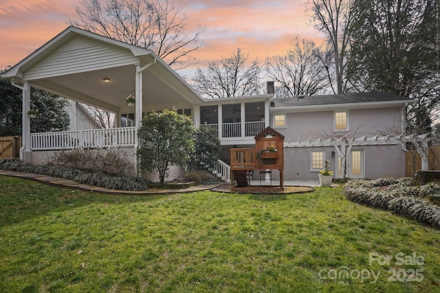 rear view of house featuring brick siding, a sunroom, stairs, a lawn, and a chimney