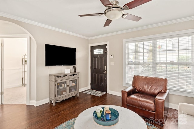 living area with arched walkways, crown molding, dark wood finished floors, ceiling fan, and baseboards