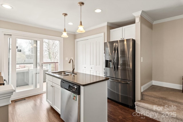 kitchen with decorative light fixtures, stainless steel appliances, a kitchen island with sink, white cabinetry, and a sink