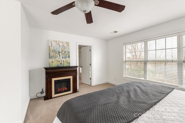 bedroom with visible vents, light carpet, ceiling fan, a warm lit fireplace, and baseboards