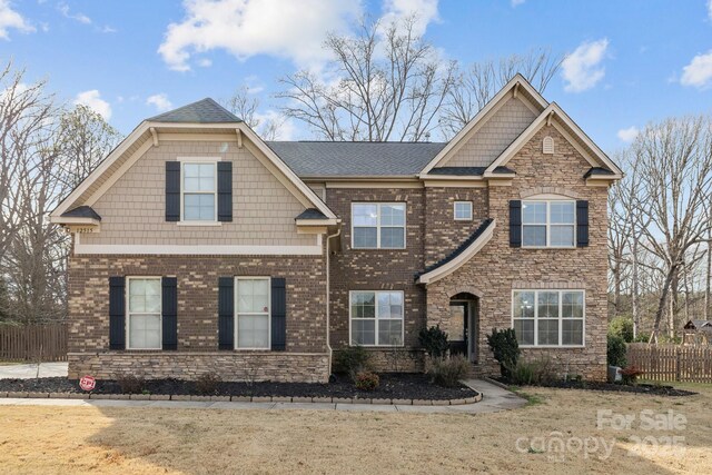 craftsman inspired home featuring a front lawn, fence, and brick siding