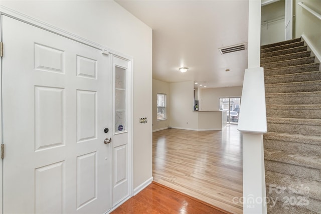 foyer featuring baseboards, stairs, visible vents, and wood finished floors