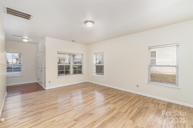 empty room with light wood-style floors, plenty of natural light, and visible vents