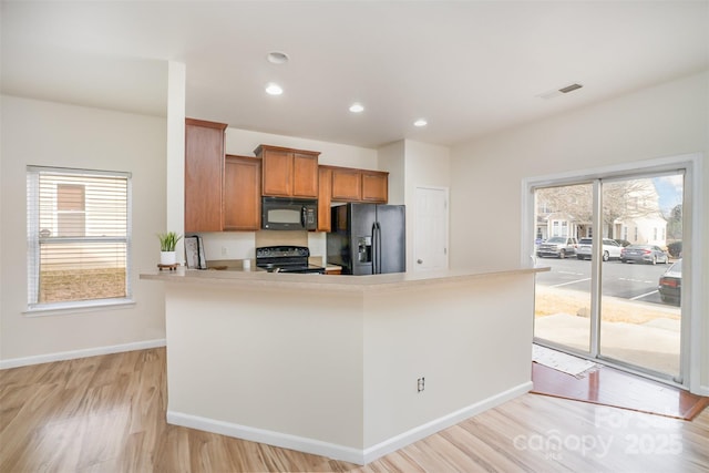 kitchen featuring brown cabinetry, light countertops, plenty of natural light, and black appliances