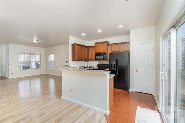 kitchen with light wood finished floors, brown cabinetry, open floor plan, a peninsula, and black appliances