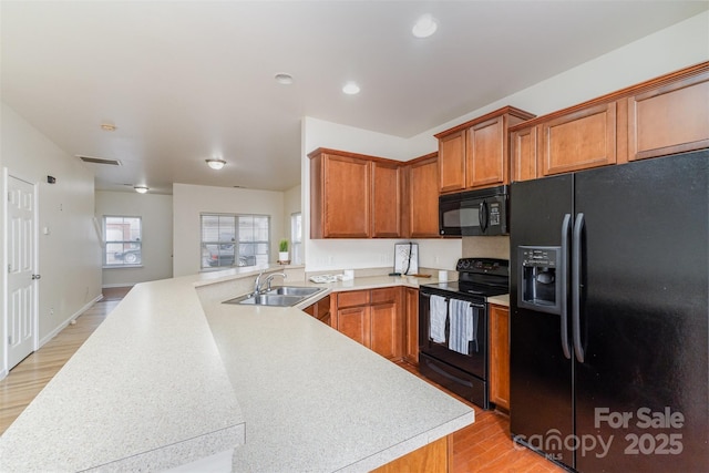 kitchen with light countertops, a sink, a peninsula, and black appliances