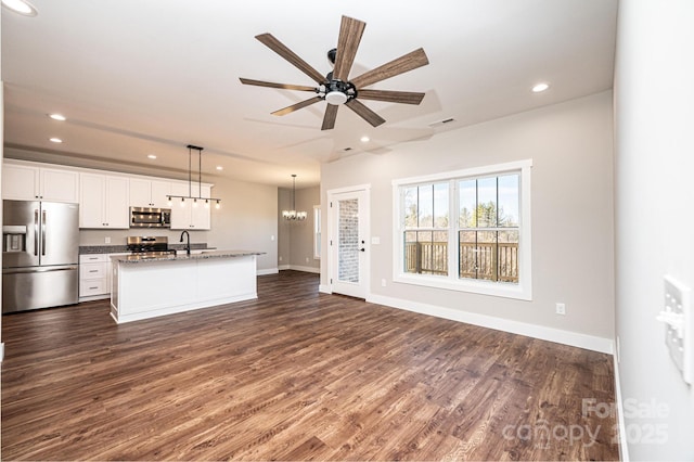 interior space featuring decorative light fixtures, white cabinetry, dark stone countertops, a kitchen island with sink, and stainless steel appliances