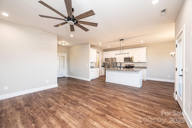 kitchen featuring white cabinetry, decorative light fixtures, appliances with stainless steel finishes, dark hardwood / wood-style floors, and an island with sink