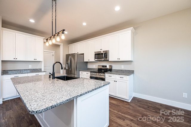 kitchen with appliances with stainless steel finishes, pendant lighting, sink, white cabinets, and a kitchen island with sink