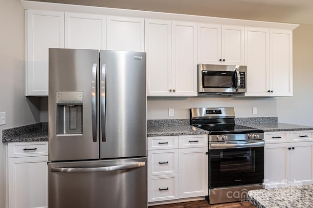 kitchen with stainless steel appliances, dark hardwood / wood-style floors, dark stone countertops, and white cabinets