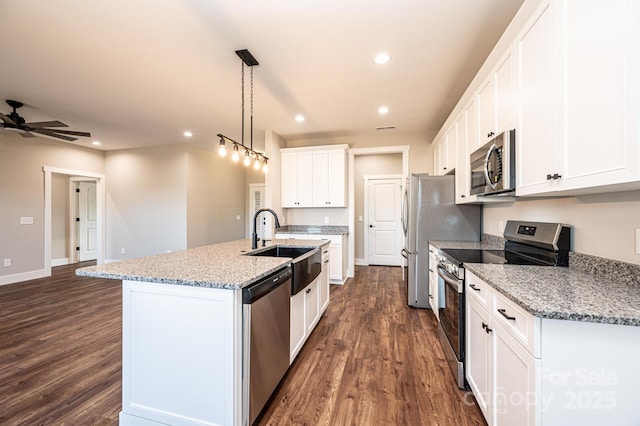 kitchen featuring white cabinetry, light stone counters, hanging light fixtures, appliances with stainless steel finishes, and a kitchen island with sink