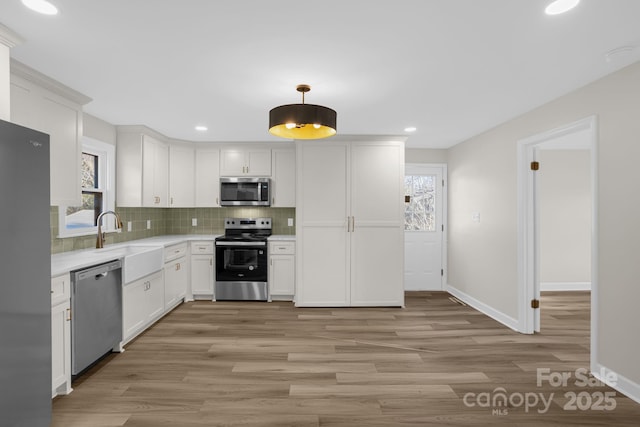 kitchen featuring sink, white cabinetry, stainless steel appliances, tasteful backsplash, and decorative light fixtures