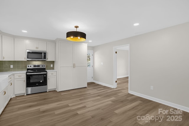 kitchen featuring hanging light fixtures, stainless steel appliances, tasteful backsplash, white cabinets, and light wood-type flooring