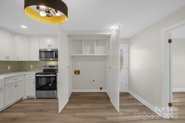 kitchen with tasteful backsplash, appliances with stainless steel finishes, white cabinets, and light hardwood / wood-style flooring