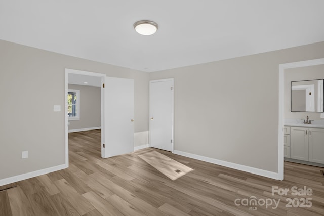 unfurnished bedroom with connected bathroom, sink, and light wood-type flooring