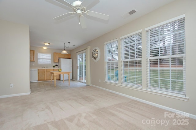 unfurnished living room with sink, a healthy amount of sunlight, light carpet, and ceiling fan