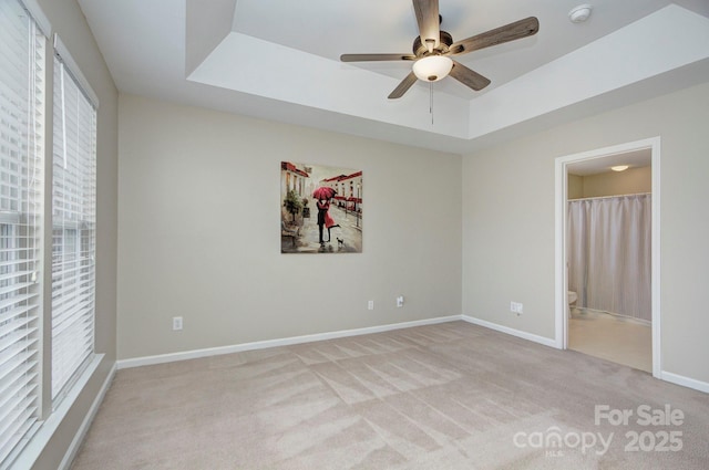 unfurnished bedroom featuring ensuite bathroom, light carpet, ceiling fan, and a tray ceiling