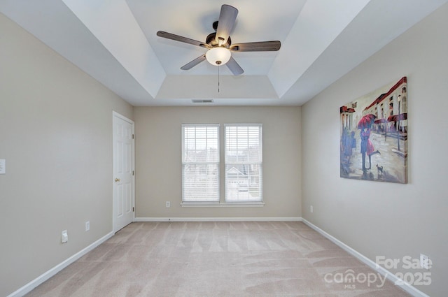 spare room featuring a raised ceiling, light colored carpet, and ceiling fan