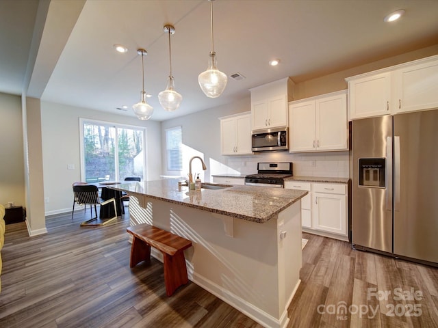 kitchen with white cabinetry, stainless steel appliances, a kitchen island with sink, and pendant lighting