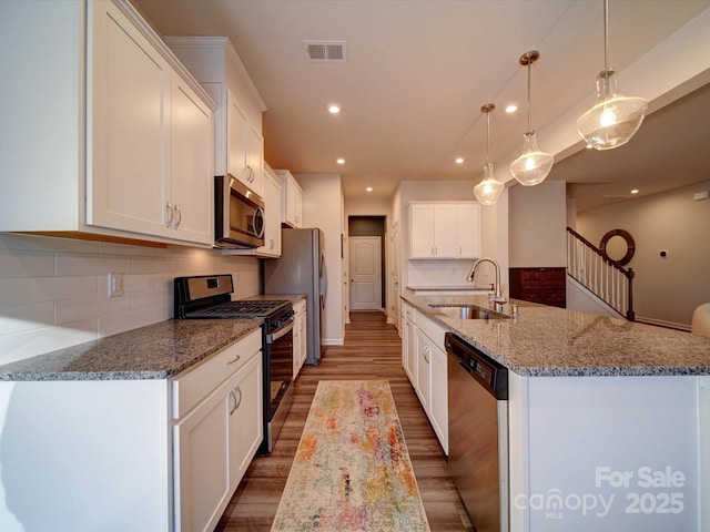 kitchen featuring sink, hanging light fixtures, stainless steel appliances, an island with sink, and white cabinets