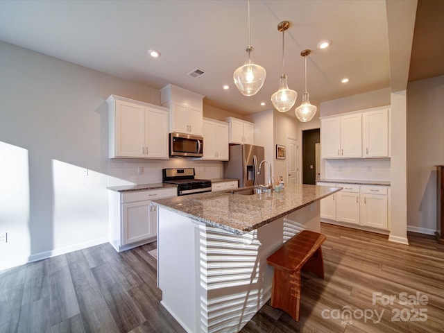 kitchen featuring hanging light fixtures, appliances with stainless steel finishes, a center island with sink, and white cabinets