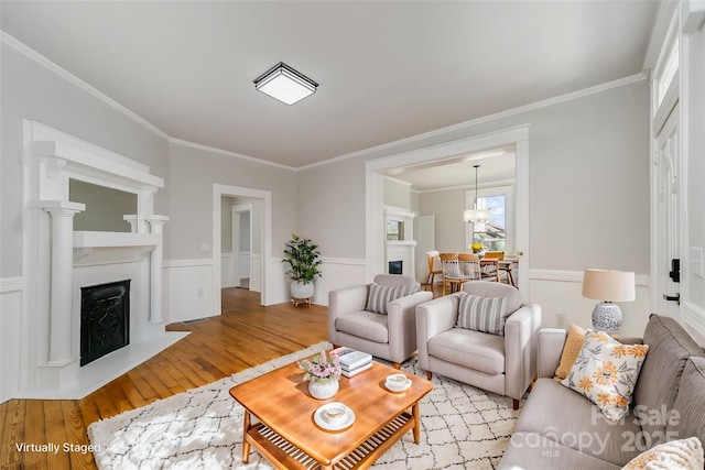 living area featuring a wainscoted wall, light wood-style flooring, a fireplace, and crown molding