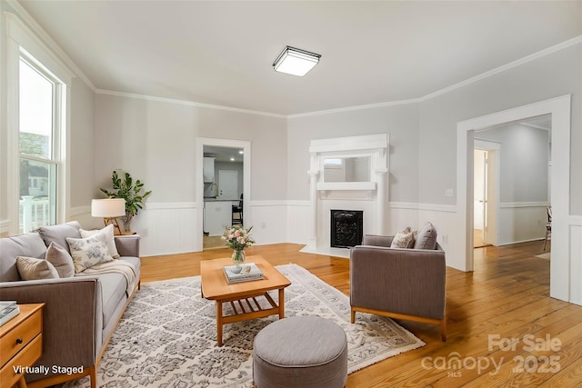 living room with a wainscoted wall, a fireplace with flush hearth, wood finished floors, and crown molding