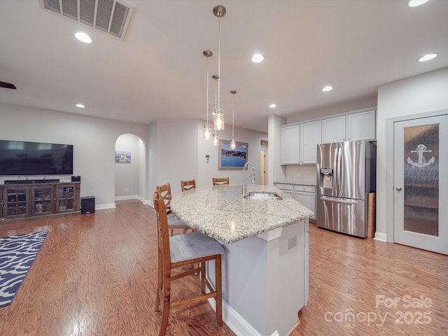 kitchen with a breakfast bar, sink, hanging light fixtures, stainless steel fridge, and white cabinets