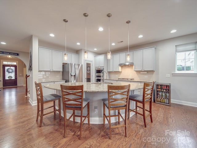 kitchen with appliances with stainless steel finishes, a kitchen island with sink, hanging light fixtures, and white cabinets