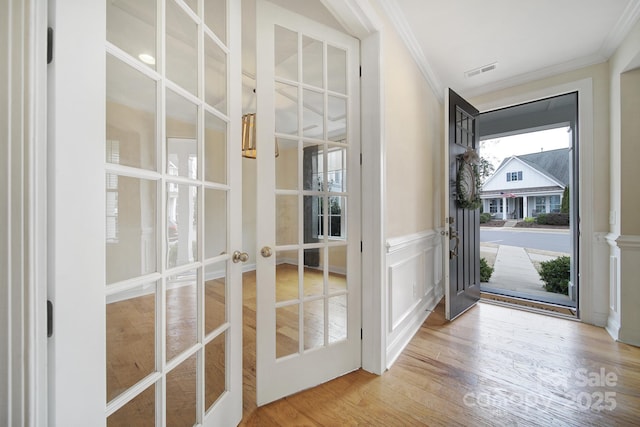 entryway with wood-type flooring, ornamental molding, and french doors