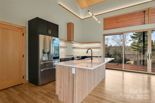 kitchen with pendant lighting, sink, a kitchen island with sink, stainless steel refrigerator with ice dispenser, and light wood-type flooring