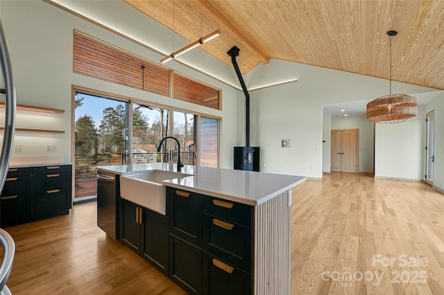 kitchen featuring sink, wood ceiling, decorative light fixtures, a wood stove, and an island with sink