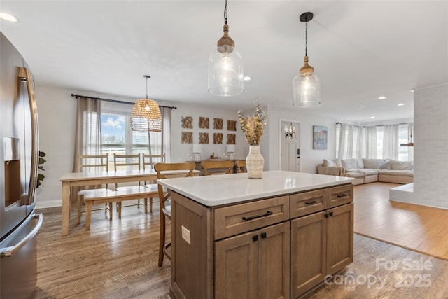 kitchen featuring decorative light fixtures, stainless steel fridge, light hardwood / wood-style floors, and a center island