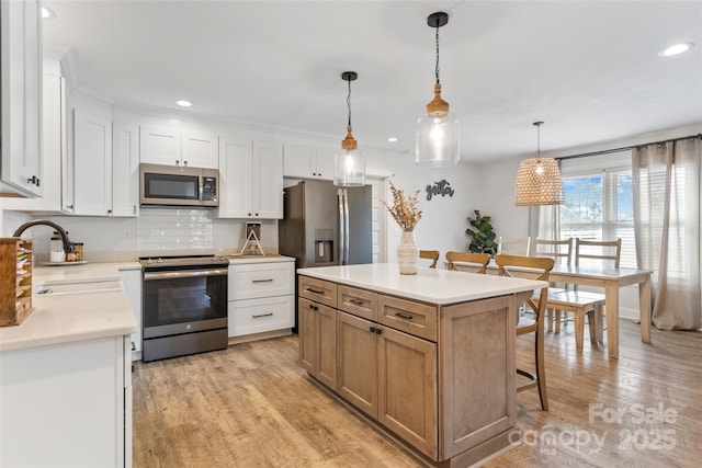 kitchen with white cabinetry, stainless steel appliances, decorative light fixtures, and a kitchen island