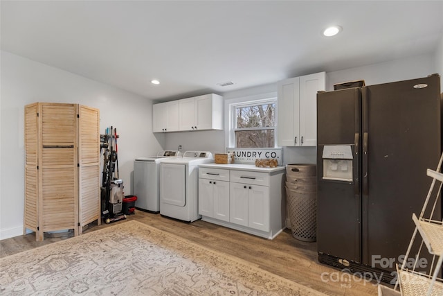 laundry room featuring separate washer and dryer, cabinets, and light wood-type flooring