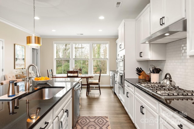 kitchen with appliances with stainless steel finishes, sink, white cabinets, decorative backsplash, and hanging light fixtures