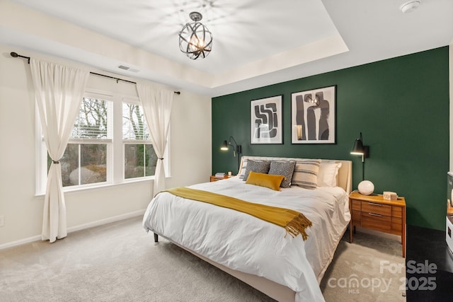 bedroom with a tray ceiling, a chandelier, and light carpet