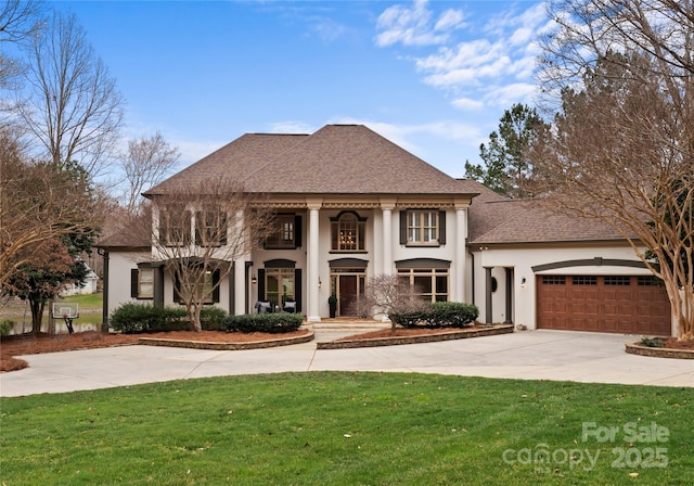 neoclassical home with stucco siding, a front lawn, concrete driveway, a shingled roof, and a garage