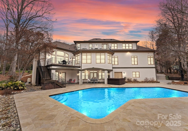 rear view of property with stucco siding, a hot tub, an outdoor pool, stairs, and a patio area