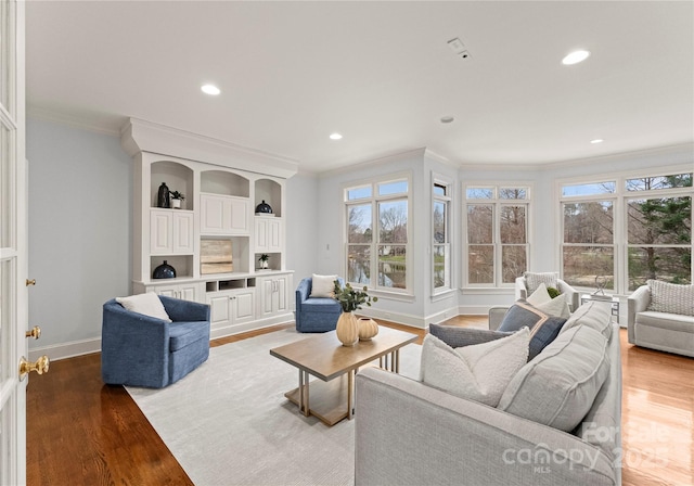 living area with baseboards, light wood-style floors, a healthy amount of sunlight, and ornamental molding