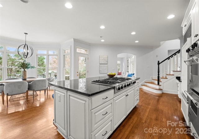 kitchen featuring arched walkways, white cabinetry, stainless steel appliances, and wood finished floors