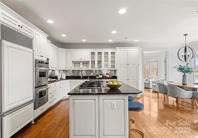 kitchen with wood finished floors, a kitchen island, a breakfast bar, white cabinets, and appliances with stainless steel finishes