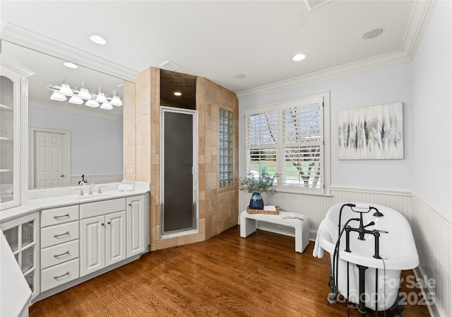 full bath featuring a wainscoted wall, a shower stall, crown molding, and wood finished floors