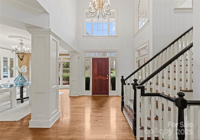 entrance foyer featuring wood finished floors, stairway, an inviting chandelier, a towering ceiling, and ornate columns