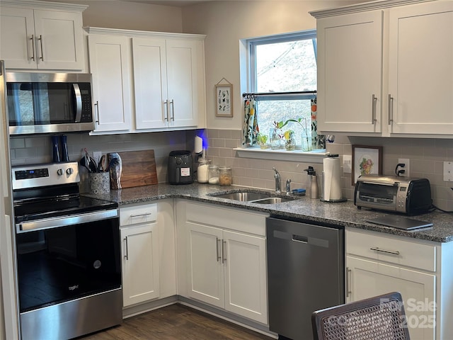 kitchen with stainless steel appliances, sink, white cabinets, and dark stone counters